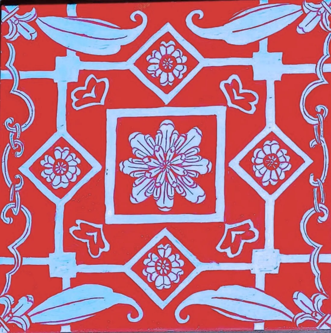 A hand-painted square tile: blue floral motifs on a red ground.
