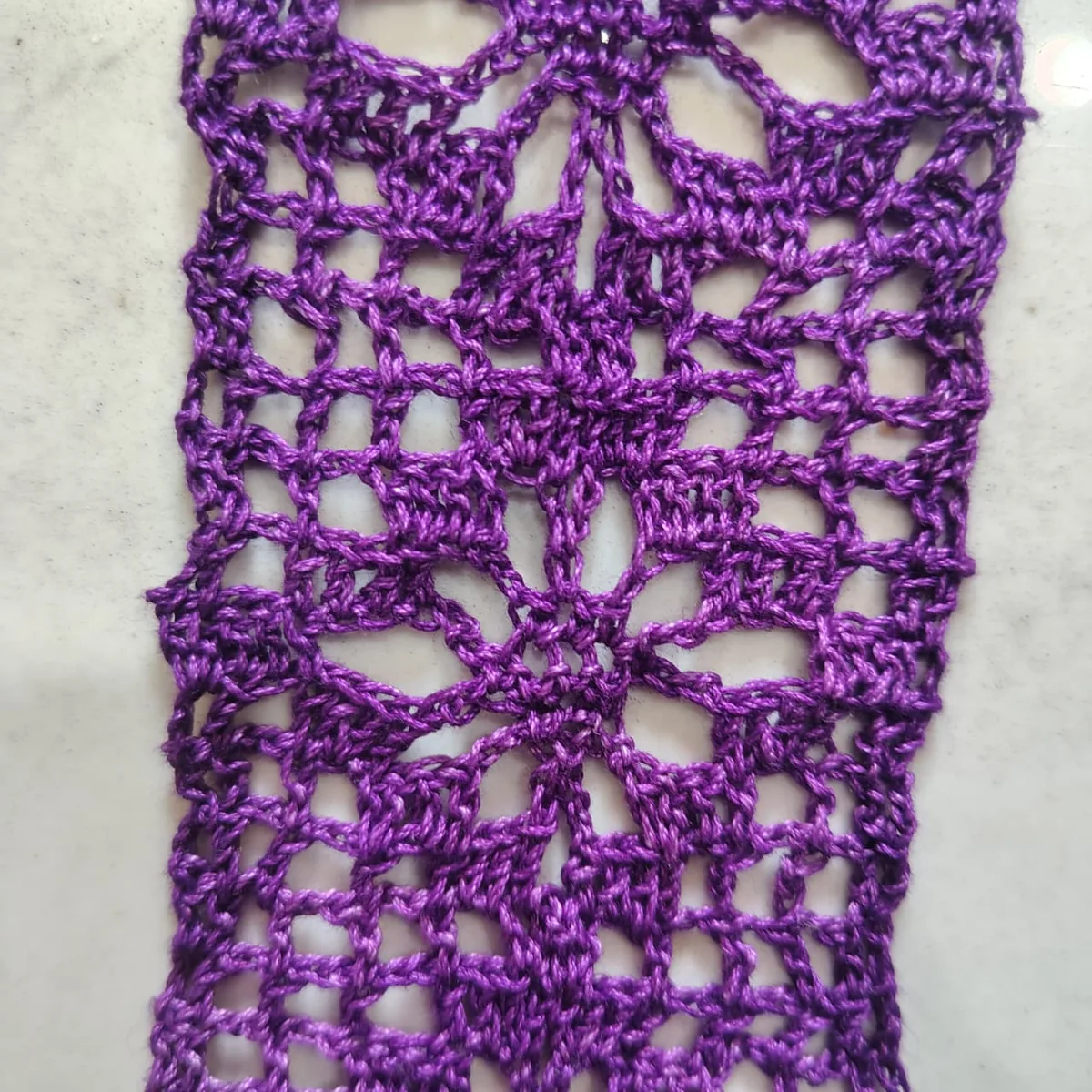Purple crochet lace, close up: rows of chain stitches open into a pattern of holes.